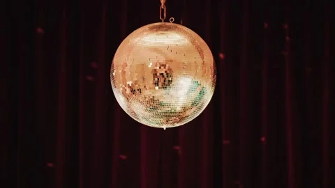 A sparkling disco ball rotates slowly against a deep red curtain background.. Stock Footage 339405626