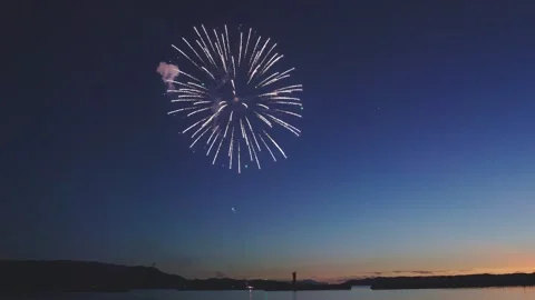 Sparkling firework burst in dusk blue sky over coastal horizon Stock Footage 340632656