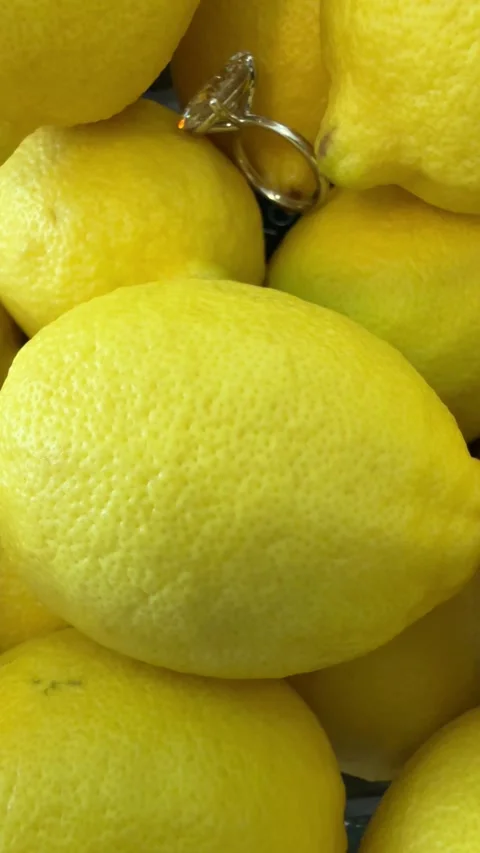 Sparkling oval diamond engagement ring shining over yellow lemons Stock Footage 320313873