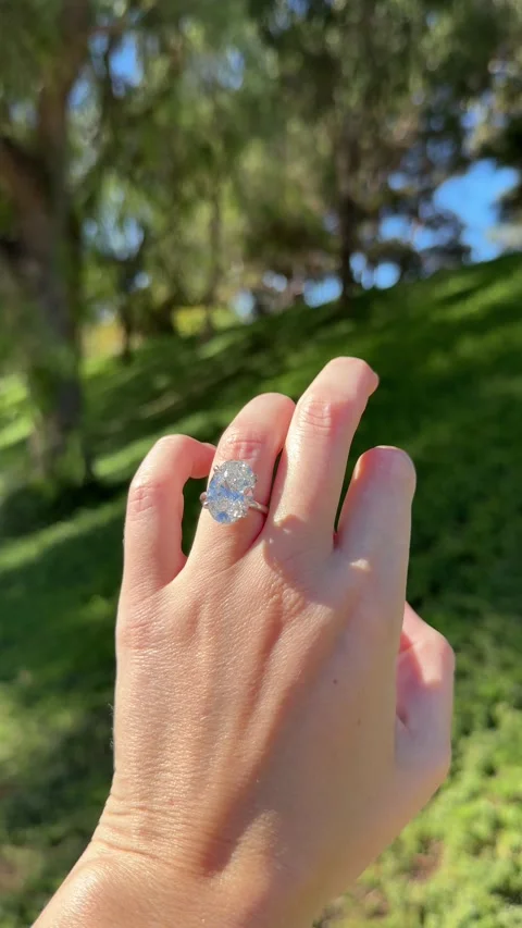 Sparkling oval diamond engagement ring in front of tall green tree branches Stock Footage 320313930