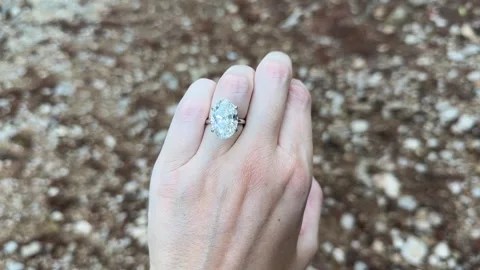 Sparkling oval diamond ring on woman’s hand against textured stone 스톡 동영상 319455923