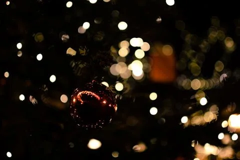 A sparkling red glitter bauble surrounded by warm golden lights against a d.. Stock Photos