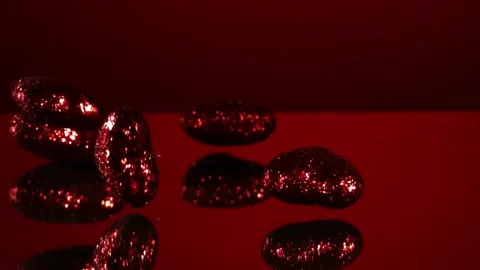 Sparkling red hearts fall and bounce on a reflective red surface. Stock Footage 326626319