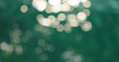 Sparkling sun highlights forming soft circular bokeh shapes on the calm emerald Stock Footage 344769996