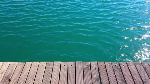 Sparkling turquoise water rippling next to a wooden pier on a sunny day 스톡 동영상 337654093