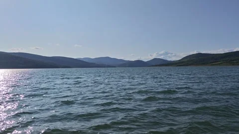 Sparkling water surface reflecting sunlight with mountains in the background Vidéo 312122818