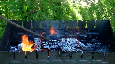 Sparks from coals fly to the sides while stirring burning wood in the grill. Stock Footage 203815970