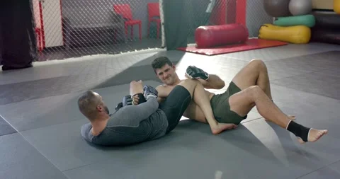 Sparring partners practicing submissions on mats in mma gym wrapping leg and Stock Footage 343238840