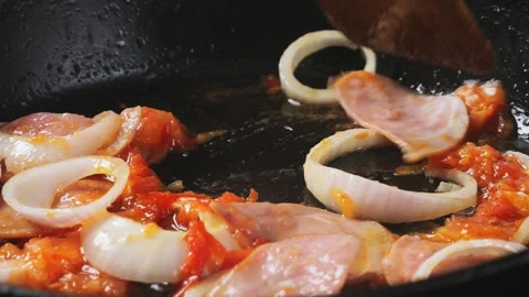 A spatula stirs fried tomatoes with ham and onions in a frying pan. Medium .. 库存影片 284031401