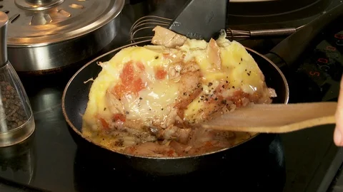 Spatulas folding or flicking a cooking omelet  in a frying pan on stovetop, Stock-Footage 128452007