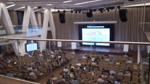 Speaker on a stage lecture for audience in big room with rows of seat. Unfocused 스톡 동영상 116777743