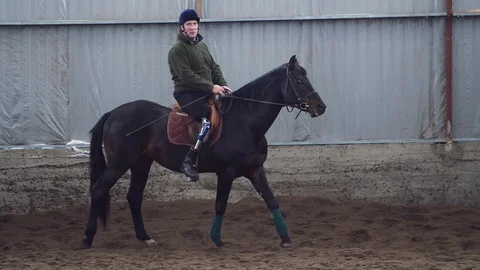 In special hangar, a young disabled man learns to ride a black, thoroughbred Stock Footage 102144495