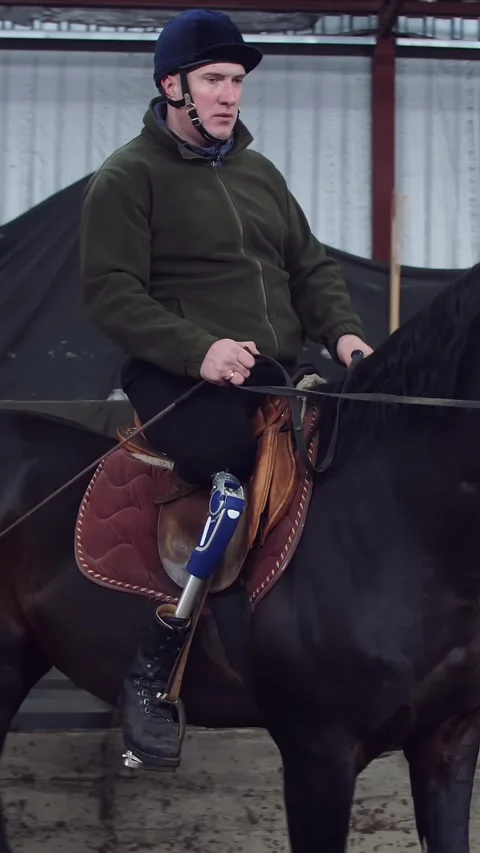In special hangar, a young disabled man learns to ride a black, Thoroughbred Stock Footage 315090859