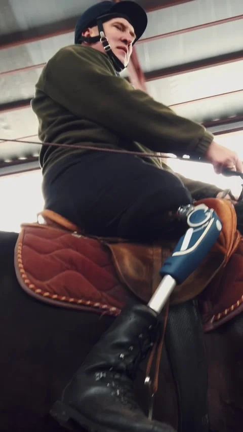 In special hangar, a young disabled man learns to ride a black, thoroughbred Stock Footage 315942986