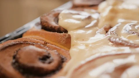 A special spatula spreading a white butter cream on fresh hot cinnamon buns with Stock Footage 106901340