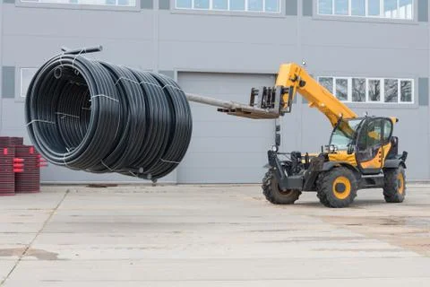 A special tractor is engaged in loading and moving pipes. Plastic pipes are t Stock Photos
