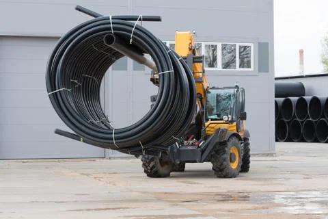 A special tractor is engaged in loading and moving pipes. Plastic pipes are t Stock Photos