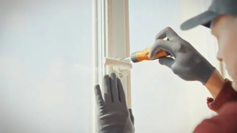 A specialist carefully adjusts plastic window hardware with a screwdriver in Stock Footage 341488940