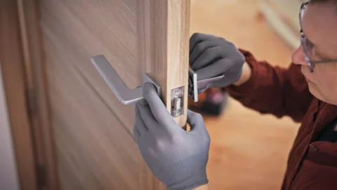A specialist in gloves and uniform fixes a door lock mechanism on a wooden i Stock Footage 342240330