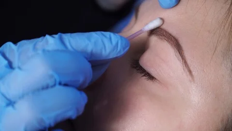 Specialist of permanent make-up wipes the face of the female patient with a Stock Footage 85619477