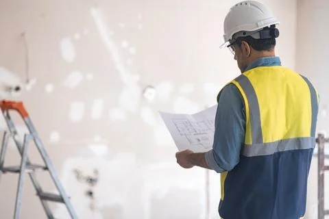 Specialist in protective hardhat looking at project plan of apartment stands in Stock Photos