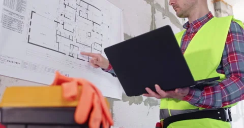 Specialist studies floor plan on wall holding computer in hands Stockbeeldmateriaal 309926795