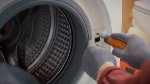 A specialist in work gloves disassembles a washing machine with a drum windo Stock Footage 340785680