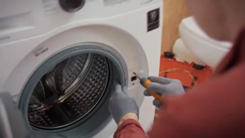 A specialist in work uniform and gloves disassembles a washing machine body Stock Footage 344877412