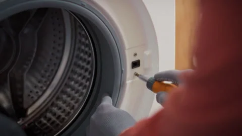 A specialist in work uniform disassembles the body of a front-loading washin Stock Footage 342240121