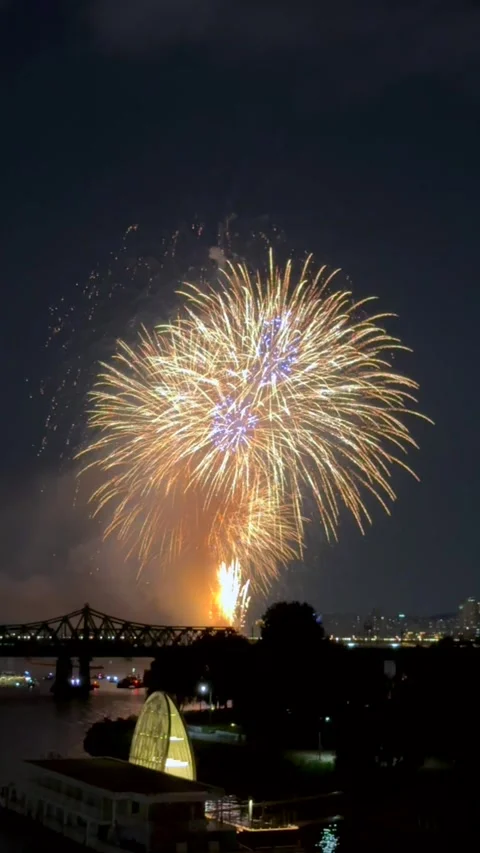 Spectacular light show with vibrant red fireworks over river bridge, turning Stock Footage 324687763
