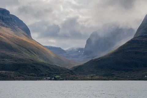 Spectacular view of valley between large mountains. A village on coastline. Stock Photos