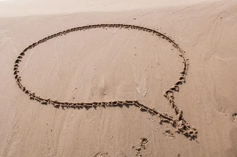 A speech or think bubble drawn out on a sandy beach. Beach background. Stock Photos