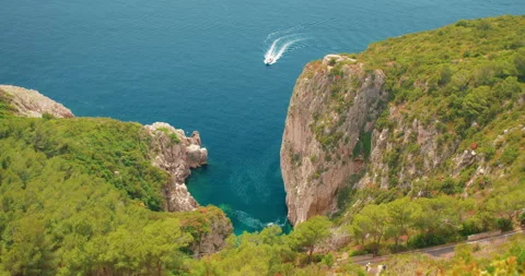 Speedboat passes through a deep blue sea near green rocky cliffs of Capri Island Stock Footage 311487914