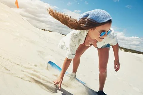 Speeding down the sand dunes. a young woman sand boarding in the desert. Stock Photos