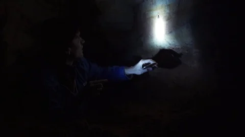 Speleologist laying on ground in cave explores cave walls with hand flashlight Stock Footage 80053529
