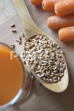 Spelt Grains On A Wooden Spoon With Carrots And Carrot Juice