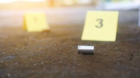 A spent bullet casing in focus, with a blurred forensic number 3 tag behind.. Stock Photos