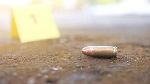 A spent bullet casing in focus, with a blurred forensic number 1 tag behind.. Stock Photos