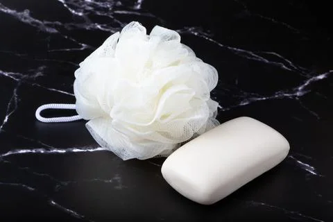 Spherical polyester bath sponge and white soap on a dark marble surface. Taking Stock Photos