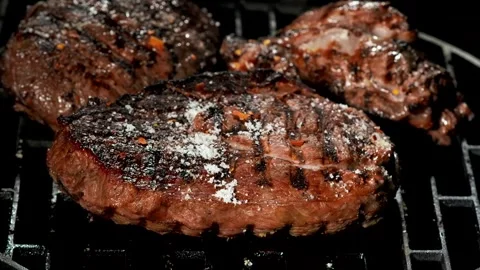 Spices fall on a grilled beef steak on a metal grate over an open fire Video stock 257683536