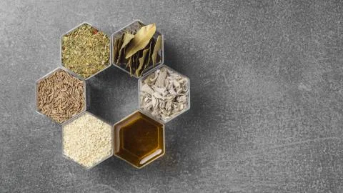 Spices in hexagonal jars appear on a gray stone surface Stock Photos