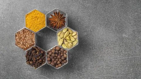 Spices in hexagonal jars appear on a gray stone surface Stock Photos