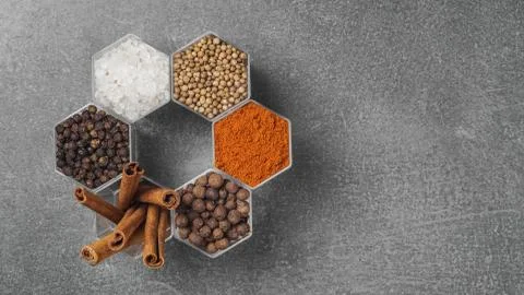 Spices in hexagonal jars appear on a gray stone surface Stock Photos