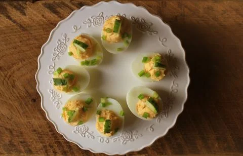 Spicy deviled eggs garnished with cucumber and leek on white plate. Top view. Stock Photos