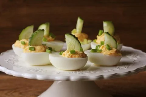 Spicy deviled eggs garnished with cucumber and leek on white plate. Wooden ru Stock Photos