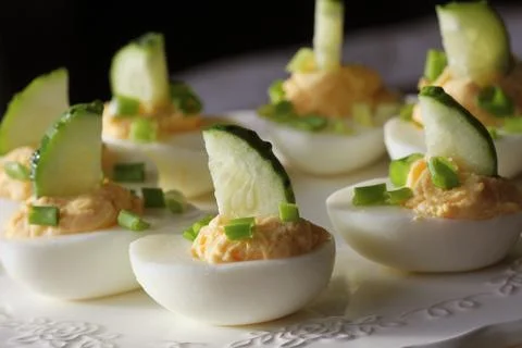 Spicy deviled eggs garnished with cucumber and leek on white plate Stock Photos