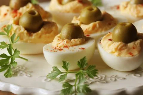 Spicy deviled eggs garnished with green olives on white plate Stock Photos