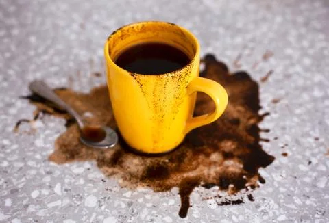Spilled coffee on kitchen table with yellow mug and teaspoon. Stock Photos