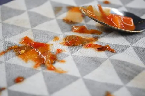 Spilled sauce on a patterned cloth with a spoon nearby Stock Photos