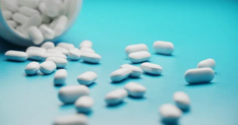 Spilling pills from white bottle on blue background - slow motion Vídeos de archivo 307948729